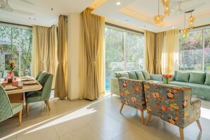 A modern living room with a dining area, large windows, and a green sofa. - Elivaas Laguna Aurelia - Goa (Vagator)