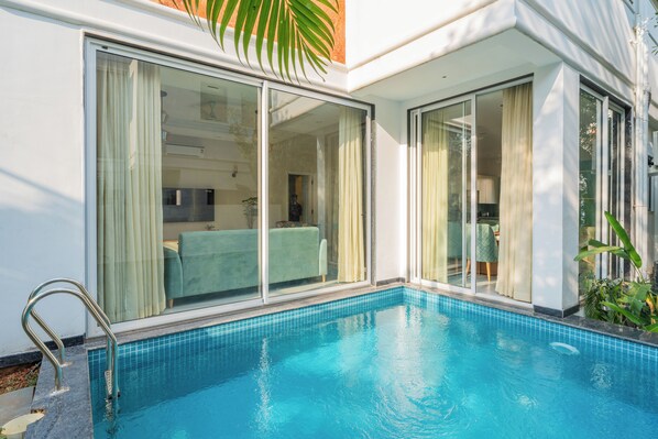 A modern hotel room with a private pool, large sliding glass doors, and a visible kitchen area. - Elivaas Laguna Aurelia - Goa (Vagator)