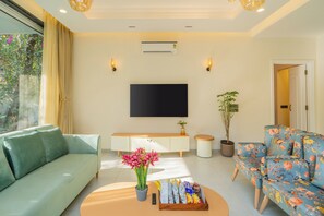 A modern living room with a sofa, a floral armchair, a coffee table, and a flat-screen TV mounted on the wall. - Elivaas Laguna Aurelia - Goa (Vagator)