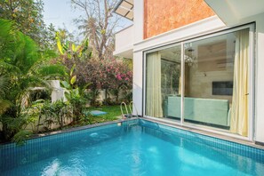 A modern hotel room with a large sliding glass door, a small pool, and lush tropical plants. - Elivaas Laguna Aurelia - Goa (Vagator)