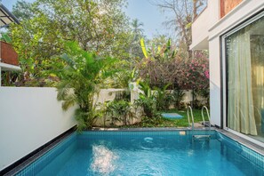 A swimming pool with a metal ladder, surrounded by lush greenery and a white wall. - Elivaas Laguna Aurelia - Goa (Vagator)