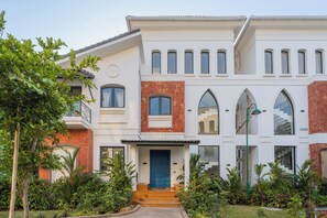 Un bâtiment à deux étages avec une porte bleue, de nombreuses fenêtres et un jardin bien entretenu.