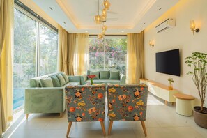 A modern living room with a sofa, two chairs, a TV, and a potted plant. - Elivaas Laguna Aurelia - Goa (Vagator)