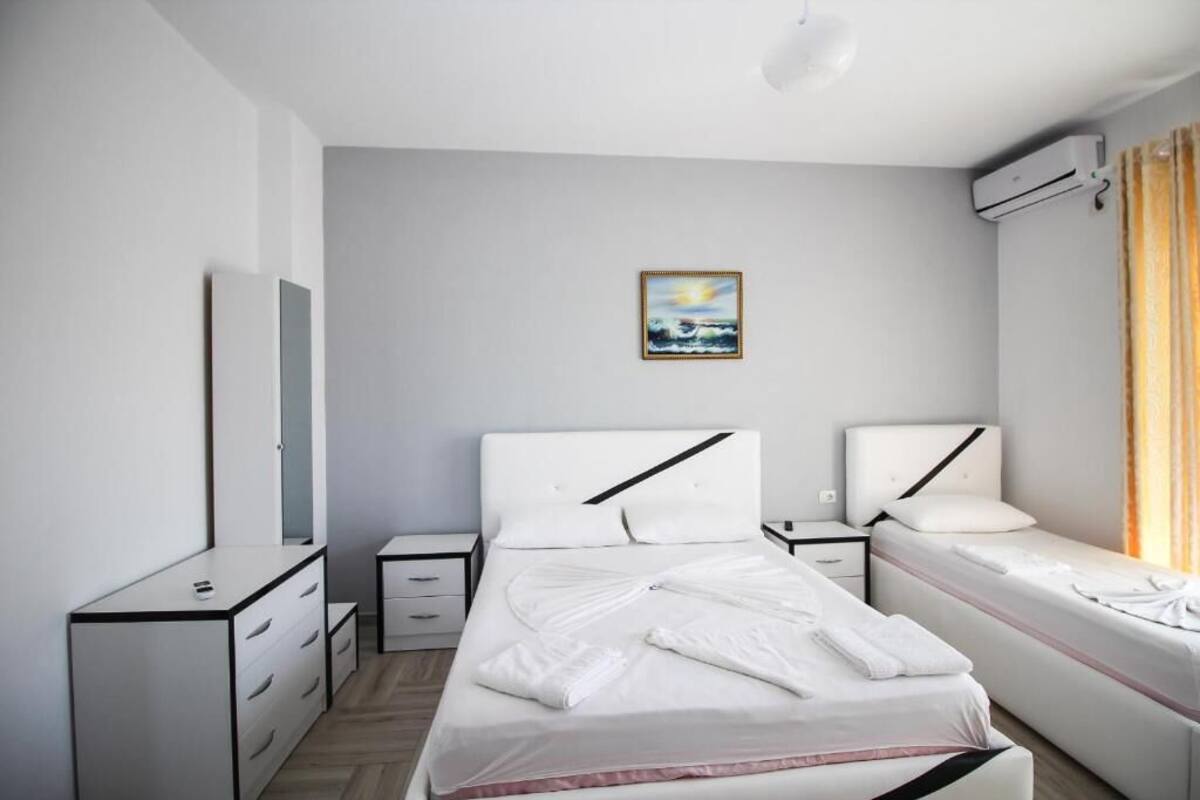 A modern hotel room with a bed, bedside tables, a dresser, and an air conditioning unit.