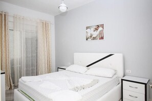 A bedroom with a bed, a nightstand, a drawer, a window with curtains, and a wall-mounted picture. - Hotel Artur 2 (Sarandë)