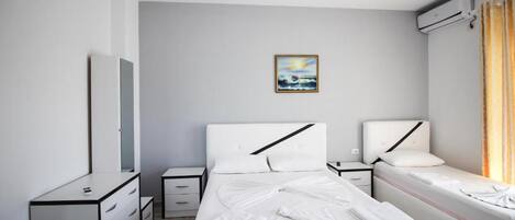 Una habitación de hotel moderna con cama, mesitas de noche, cómoda y unidad de aire acondicionado.