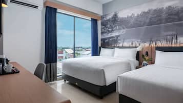 A hotel room with two beds, a desk, and a large window offering a city view.
