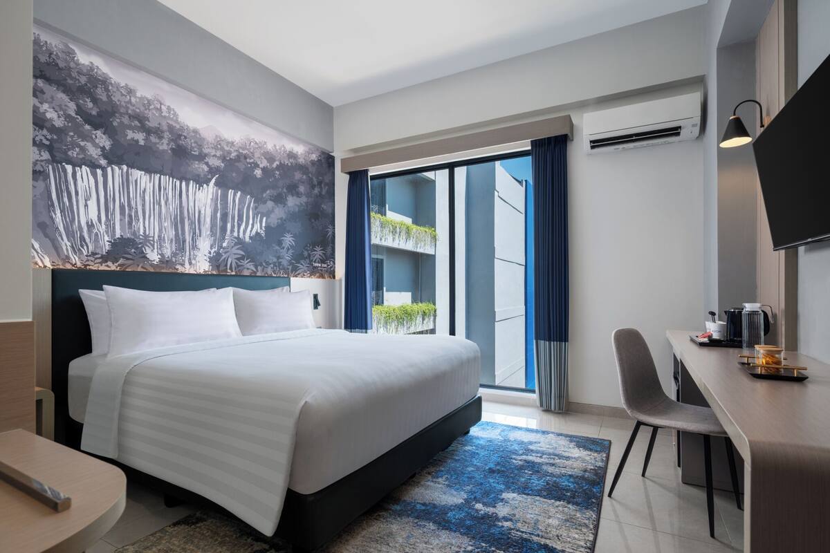 Una habitación de hotel moderna con una cama grande, un escritorio, un televisor de pantalla plana y un balcón con plantas.