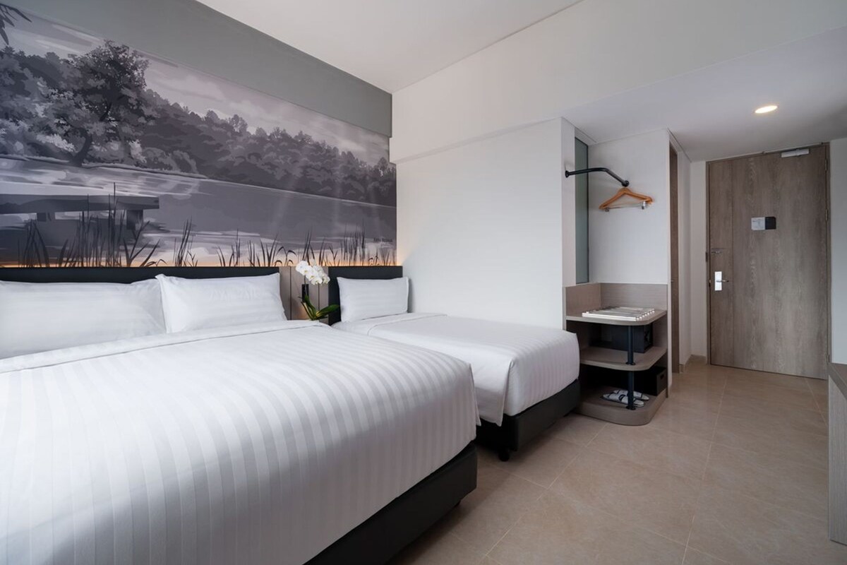 A modern hotel room with a large bed, a painting of a landscape, a small bathroom, and a wooden door.