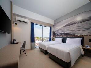 A hotel room with two beds, a desk, a chair, a TV, and a large window with a view of the city. - Aston Inn Lumajang - East Java (Lumajang)