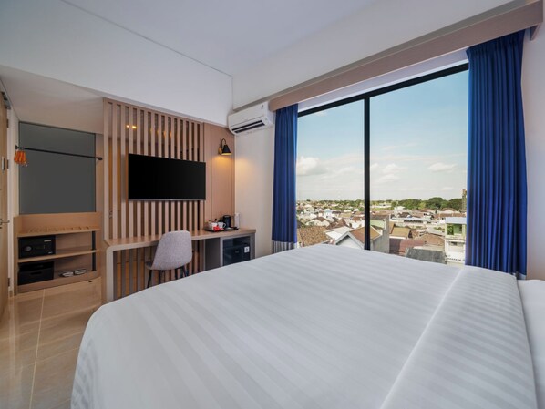 A hotel room with a large bed, a desk with a chair, a flat-screen TV, and a large window with a city view. - Aston Inn Lumajang - East Java (Lumajang)