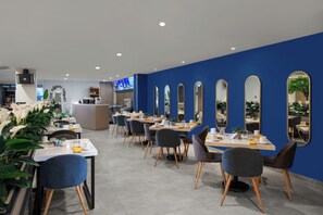 A modern dining area with tables and chairs, a reception desk, and a blue accent wall. - Aston Inn Lumajang - East Java (Lumajang)