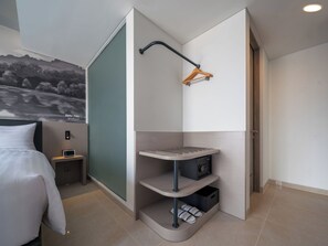 A modern hotel room with a curved corner design, a bed, a small bedside table with a lamp, a wall-mounted radio, and a shoe storage unit. - Aston Inn Lumajang - East Java (Lumajang)