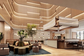 A modern hotel lobby with a central seating area, a staircase, and a reception desk.