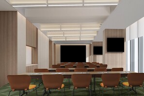 Un salón de conferencias con una mesa larga, múltiples sillas, una pantalla grande y un televisor en la pared.