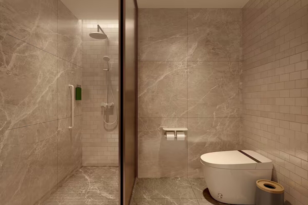 Un baño moderno con cabina de ducha de vidrio, inodoro y un pequeño cubo de basura.
