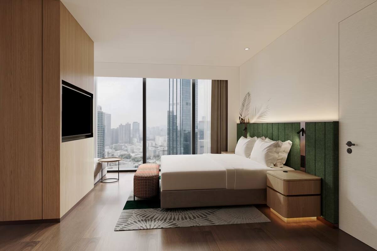 Une chambre moderne avec un grand lit, un téléviseur fixé au mur, une table de chevet et une vue sur le paysage urbain.