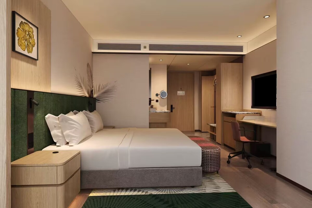 A modern hotel room with a bed, bedside table, desk, chair, and a television.