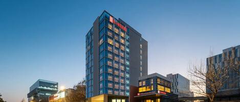 A modern hotel with multiple floors, a prominent red sign, and a well-lit facade.