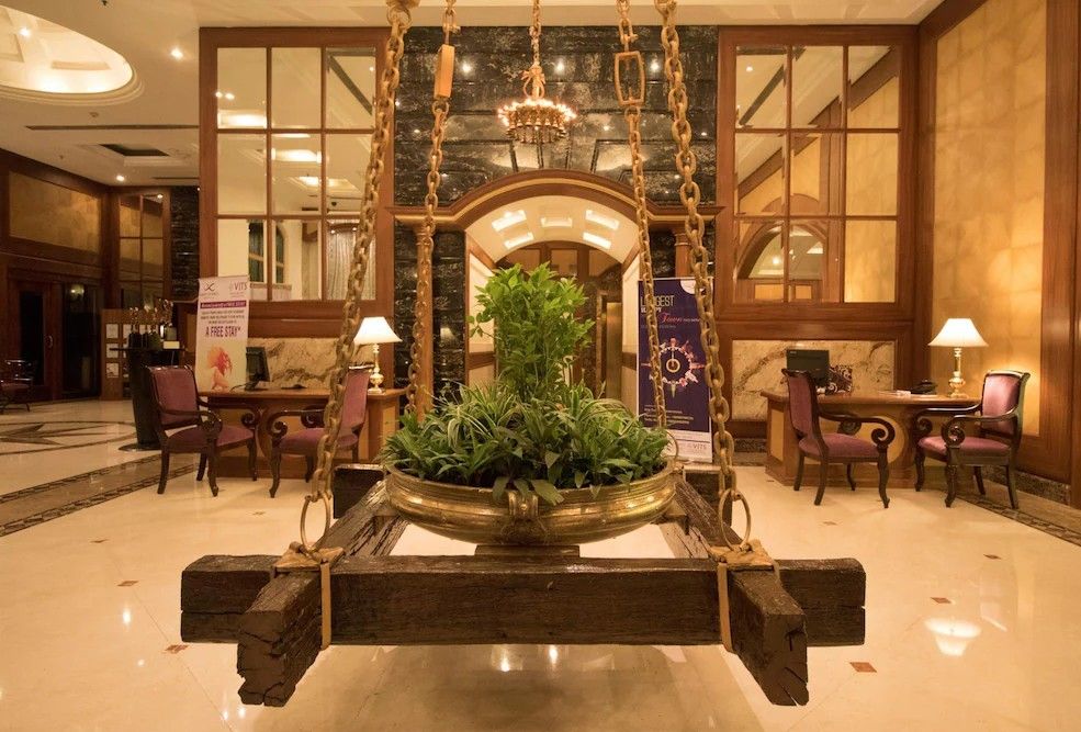 Un hall d’entrée avec un fauteuil suspendu au centre, un lustre et une grande plante en pot.