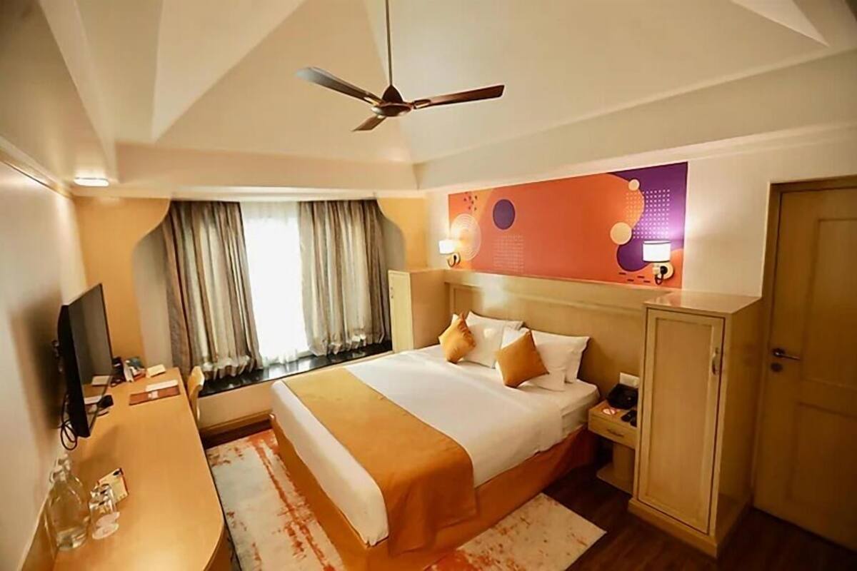 Ein Hotelzimmer mit einem Bett, einem Schreibtisch, einem Fernseher, einem Kleiderschrank und einem Deckenventilator.