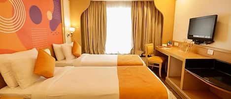 A hotel room with two beds, a desk, a television, and a large window with curtains.