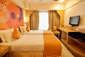A hotel room with two beds, a desk, a television, and a large window with curtains. - Ira By Orchid Mumbai - T2 International Airport (Mumbai)