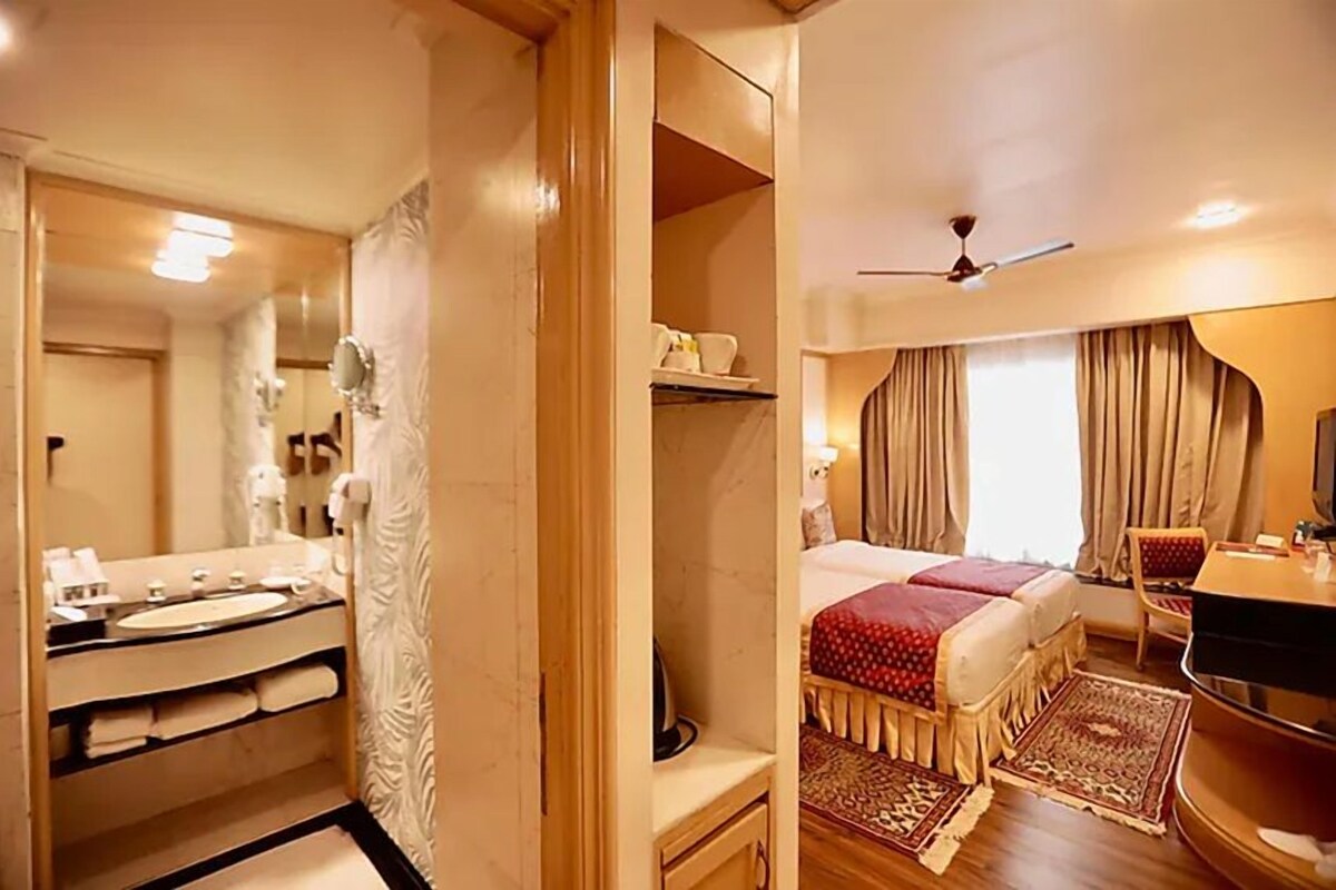 A hotel room with a bathroom, a bed with a red bedspread, a TV, and a ceiling fan.