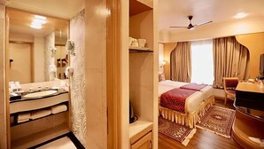 A hotel room with a bathroom, a bed with a red bedspread, a TV, and a ceiling fan. - Ira By Orchid Mumbai - T2 International Airport (Mumbai)