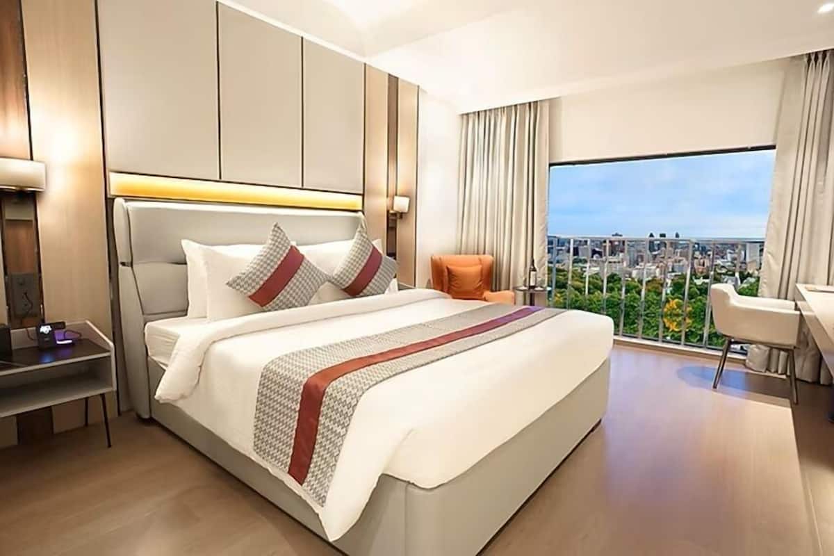 A modern hotel room with a large bed, a desk, and a view of the city.