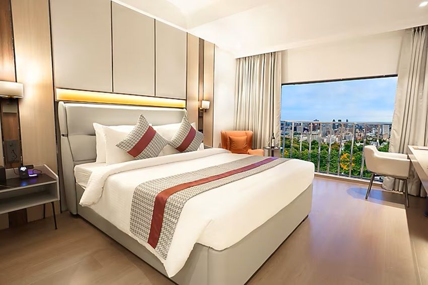 A modern hotel room with a large bed, a desk, and a view of the city.