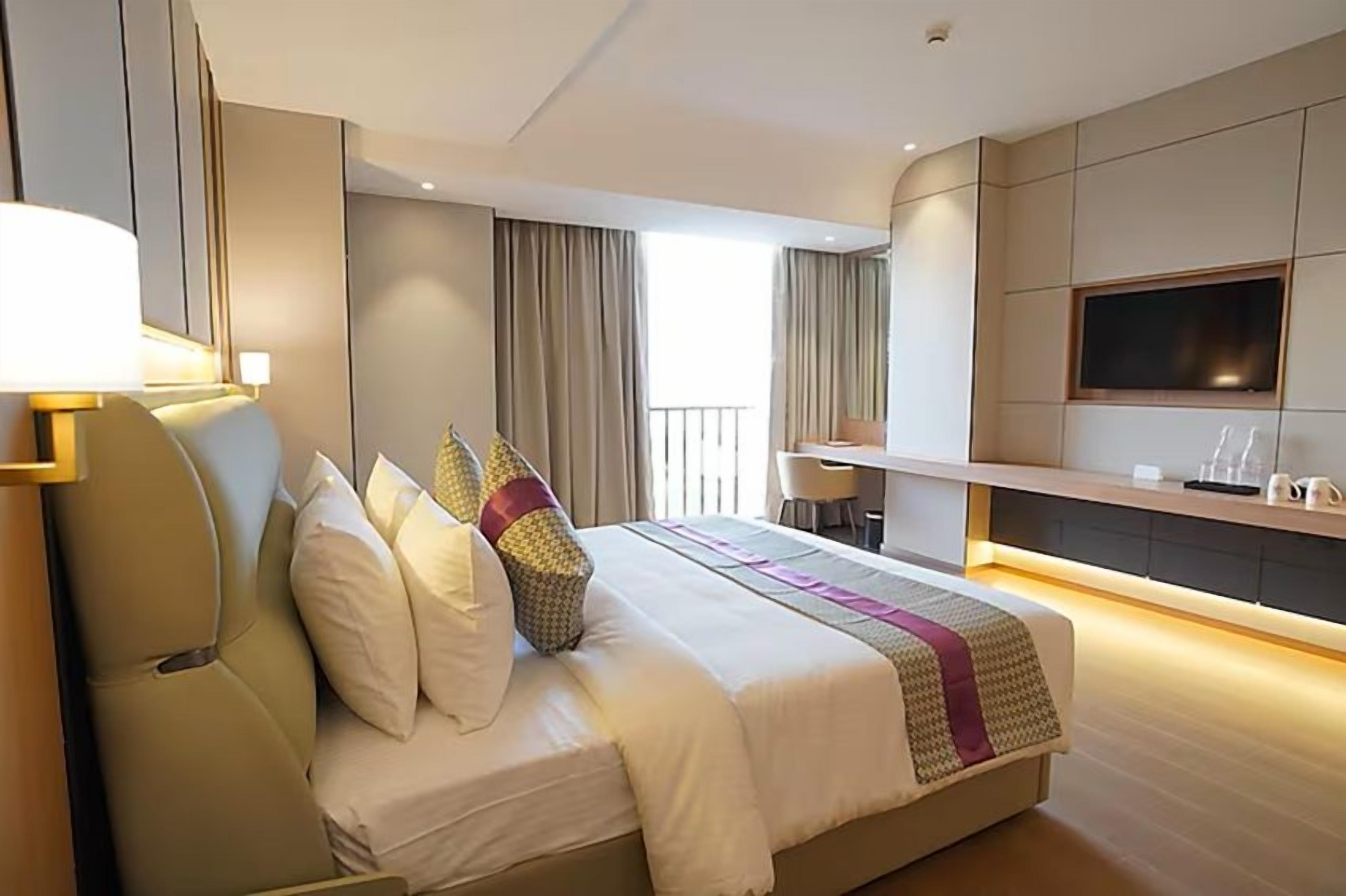 Una habitación de hotel moderna con una cama grande, un escritorio, un televisor y un balcón con cortinas.