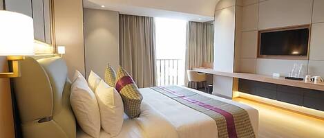 Una habitación de hotel moderna con una cama grande, un escritorio, un televisor y un balcón con cortinas.