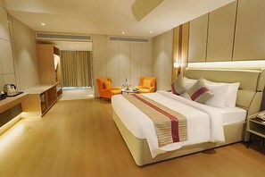 A hotel room with a large bed, two orange chairs, a small round table, and a desk with a kettle. - The Orchid Chandigarh (Dera Bassi)