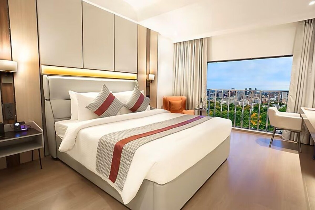 A modern hotel room with a large bed, a desk, and a view of the city.