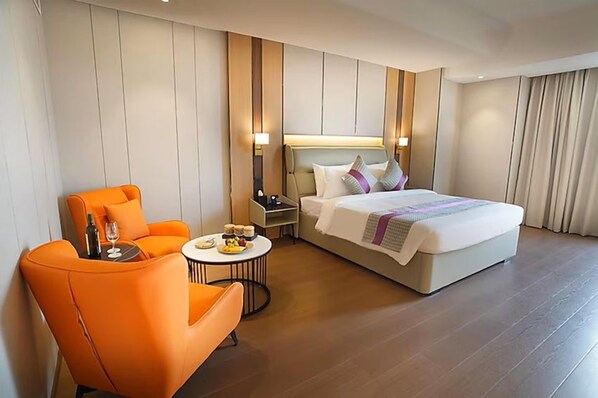 Une chambre d’hôtel avec un lit, un fauteuil orange, une petite table ronde avec une bouteille et des verres, et une table de chevet avec une lampe.