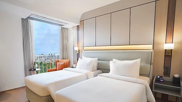 Une chambre d’hôtel avec deux lits, une vue sur la ville et un balcon avec une chaise.
