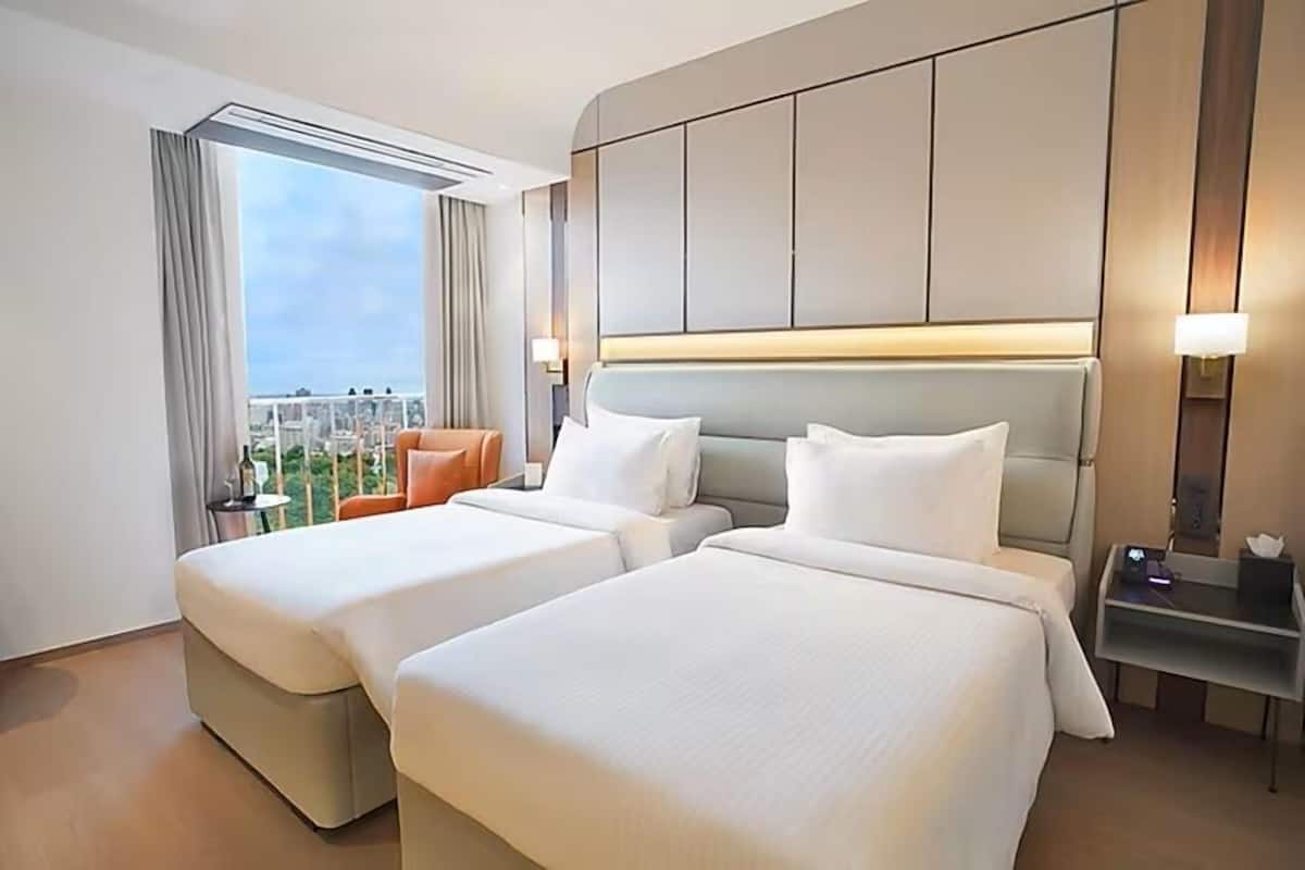 A hotel room with two beds, a view of the city, and a balcony with a chair.