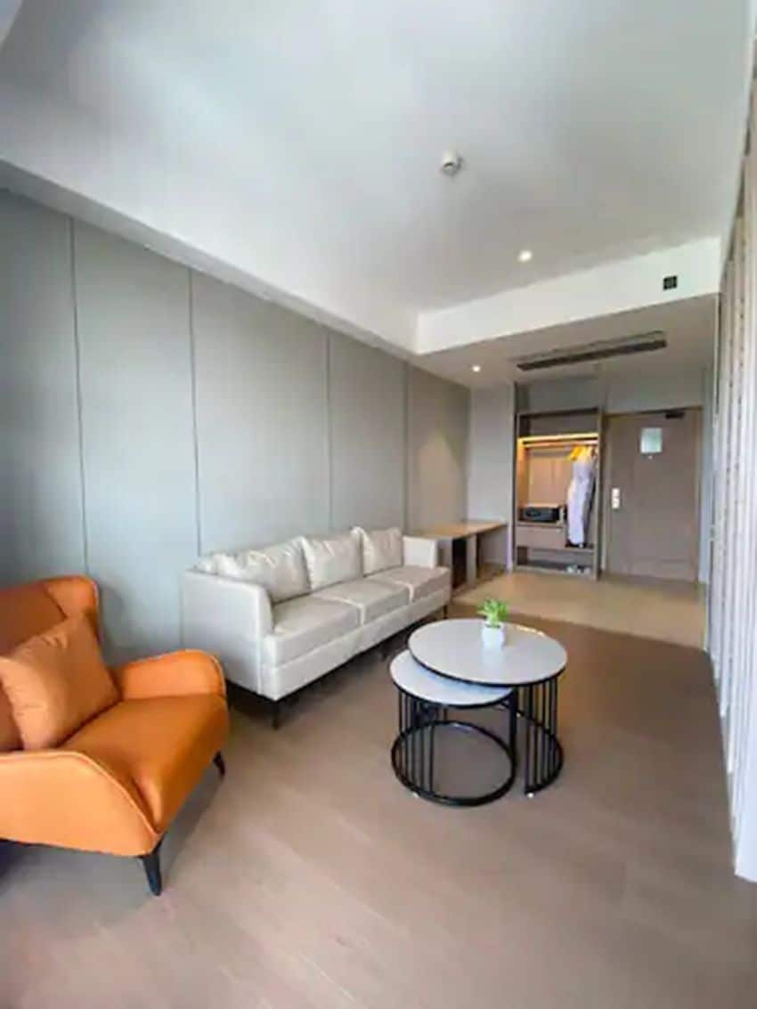 Una sala de estar moderna con un sofá blanco, un sillón naranja y una mesa de centro redonda.