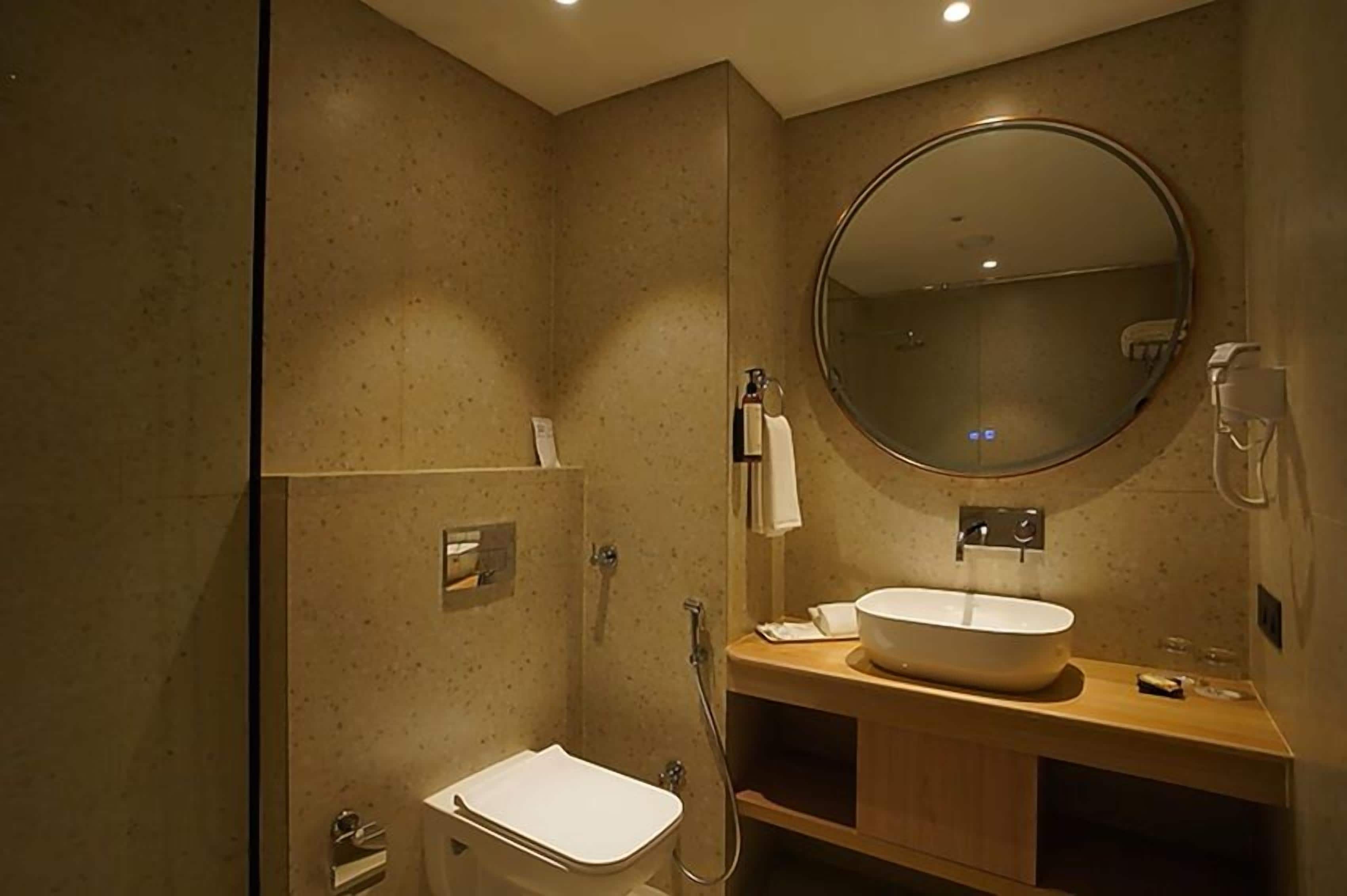 Un baño moderno con un espejo redondo grande, un lavabo blanco y una zona de ducha.