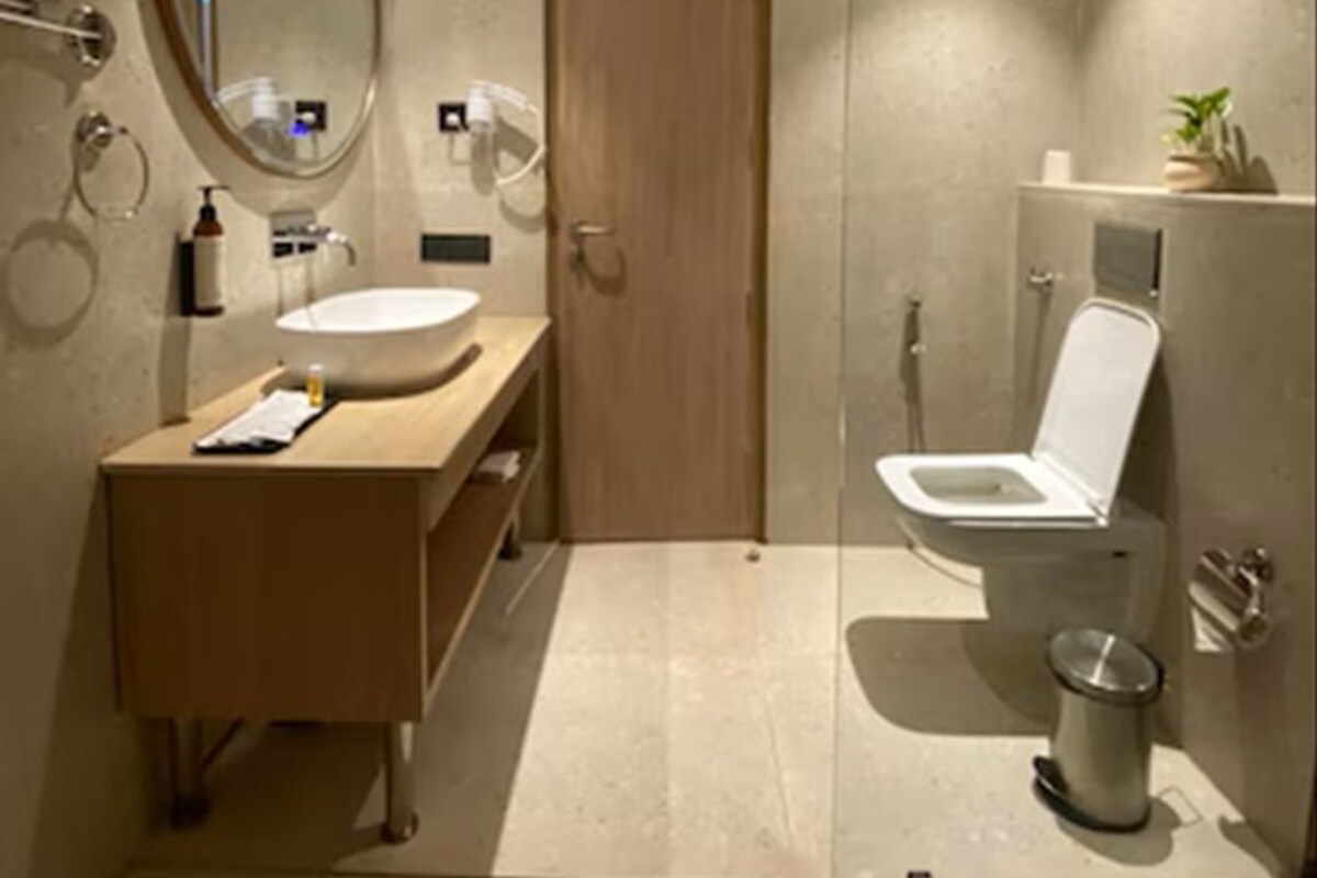 Un bagno moderno con cabina doccia in vetro, mobile bagno in legno, specchio rotondo e water.