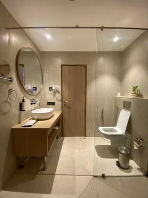 Un bagno moderno con cabina doccia in vetro, mobile bagno in legno, specchio rotondo e water.
