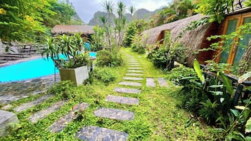 A pathway leading to a pool surrounded by lush greenery and thatched-roof structures.
