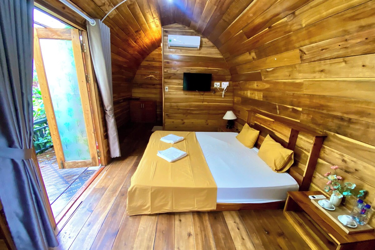 A wooden cabin bedroom with a bed, a nightstand, and a window.