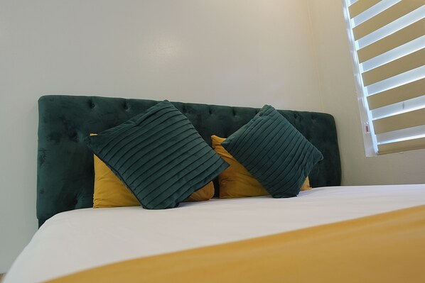 A bed with a green upholstered headboard, two dark green pillows, and a mustard-colored pillow. - Catba Backpackers Hostel & Pool Bar (Hi Phòng)