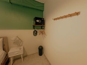 A small room with a bed, a nightstand, a trash bin, a coat rack, and a small shelf with a safe. - Viajero Panama (Panama City)