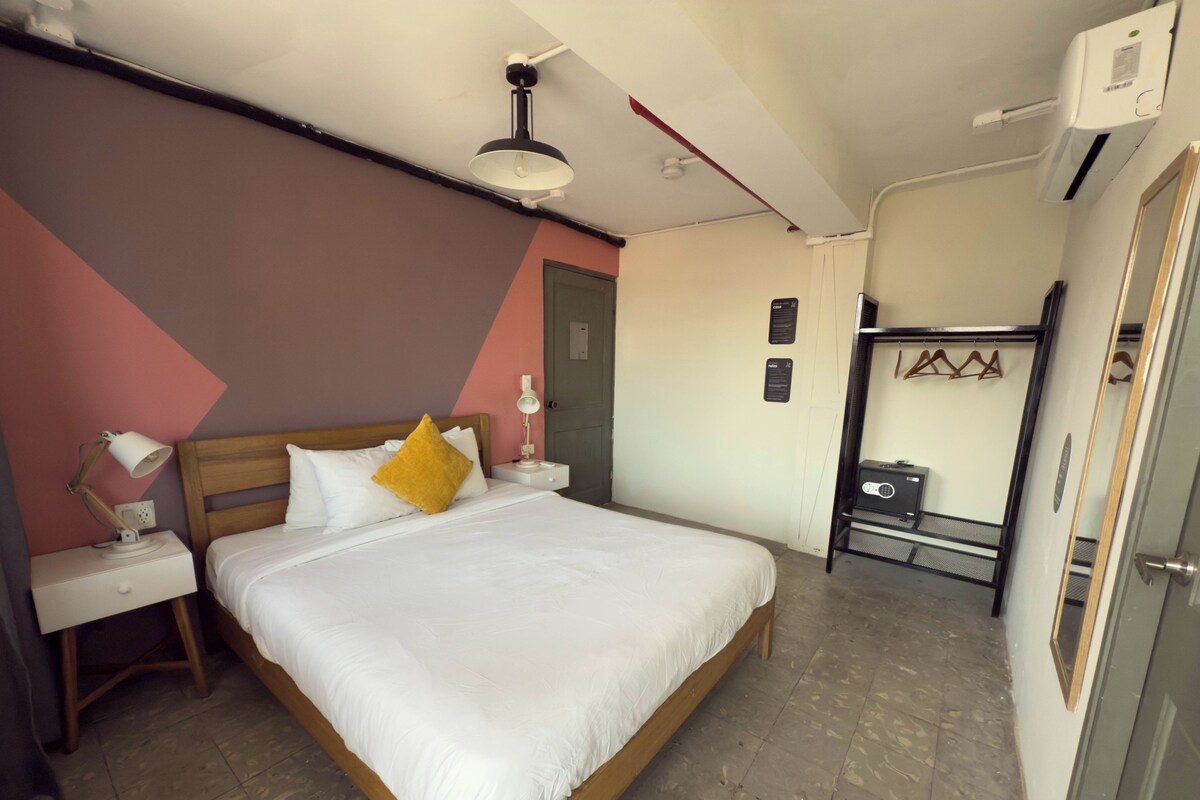 Un dormitorio ordenado con una cama de madera, ropa de cama blanca, una lámpara de noche y una mesita con lámpara.