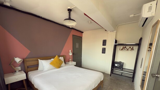 Een netjes ingerichte slaapkamer met een houten bed, witte beddengoed, een bedlampje en een klein tafeltje met een lamp.