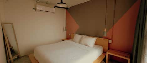 A bedroom with a large bed, a wooden headboard, a bedside table, a hanging light, and a wall-mounted air conditioner.