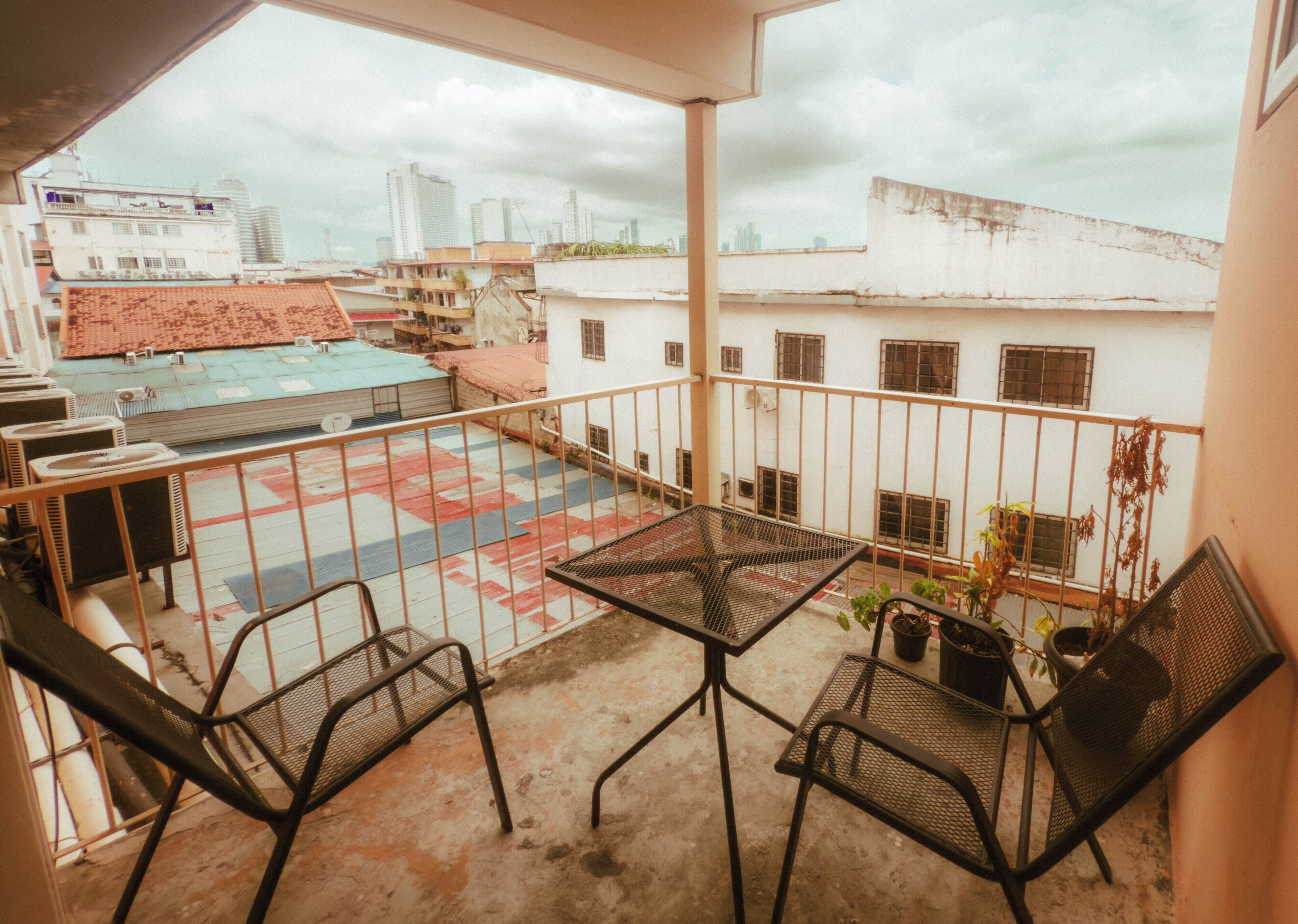 A balcony with a table and chairs, overlooking a courtyard with buildings and a cityscape.